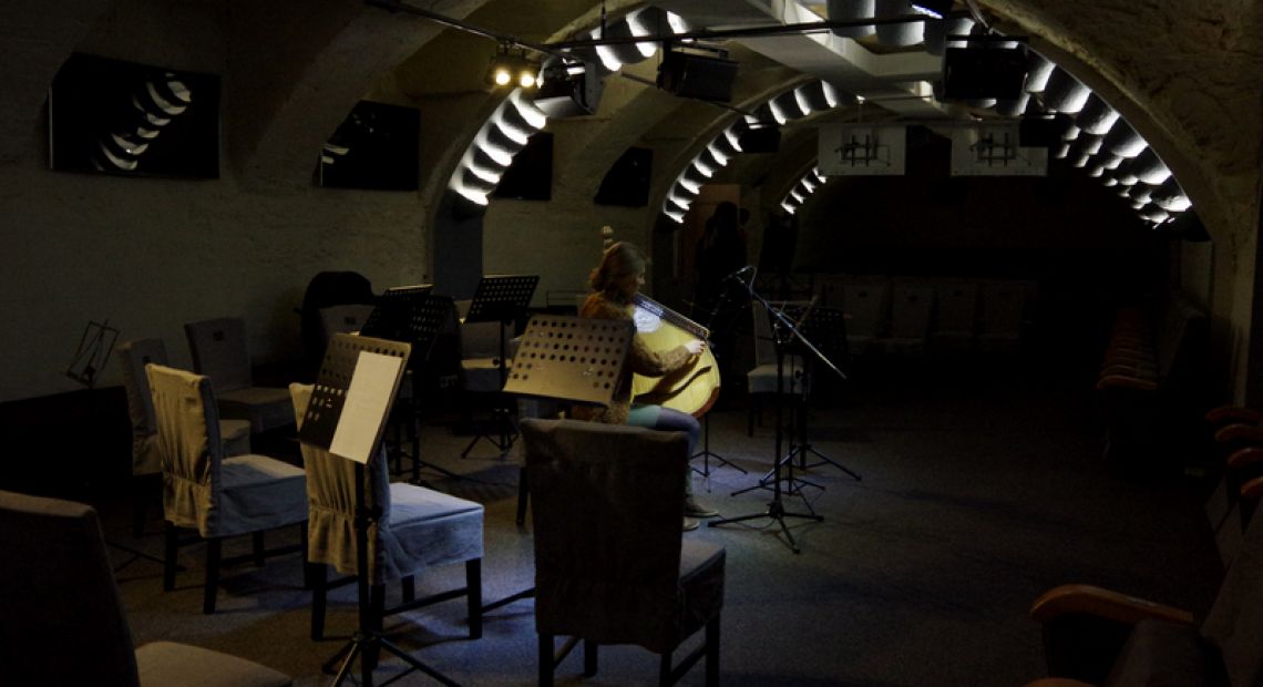 musician playing on string instrument in dark concert hall with chairs
