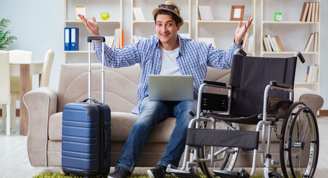 man with wheelchair and laptop in hotel room