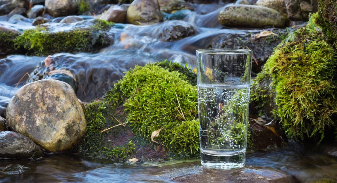 glass of water with stones and waterfall on background