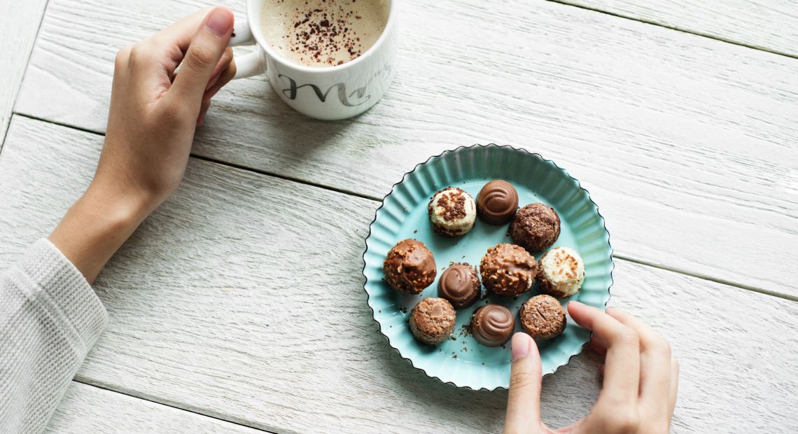 Person picking sweets and holding a cup of coffee
