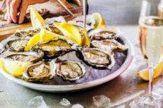 hand on table near plate with oysters served with lemon and glass of sparkling wine