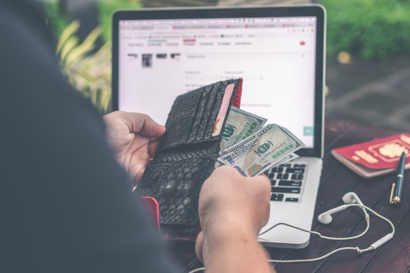 Person counting money in front of a laptop